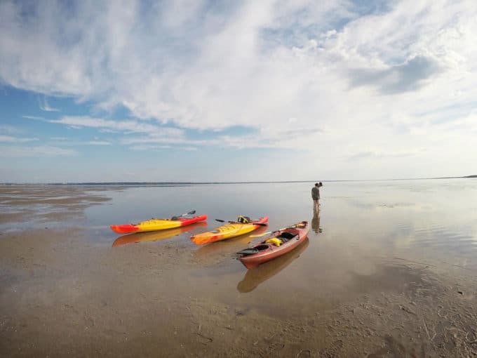 Kayaks on the mud flats of Caraquet, with one person looking out into the distance.