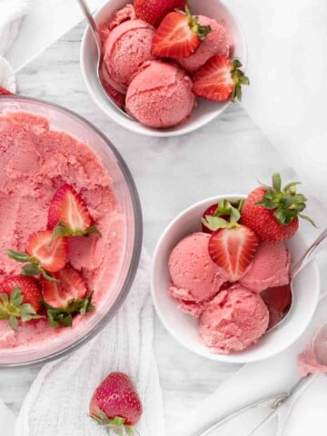 overhead view of 2 bowls of scoops of strawberry gelato next to container of frozen gelato