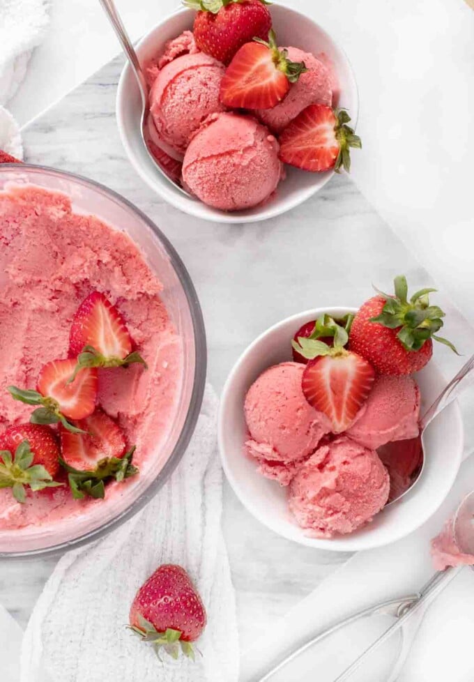 overhead view of 2 bowls of scoops of strawberry gelato next to container of frozen gelato