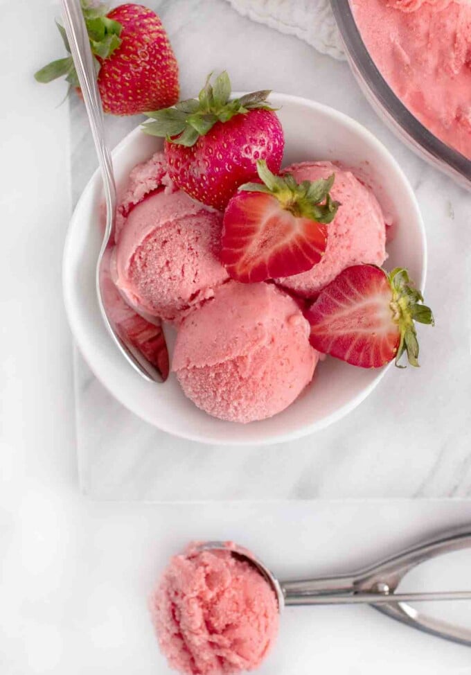 overhead view of bowl of scoops of strawberry gelato next to scooper of gelato