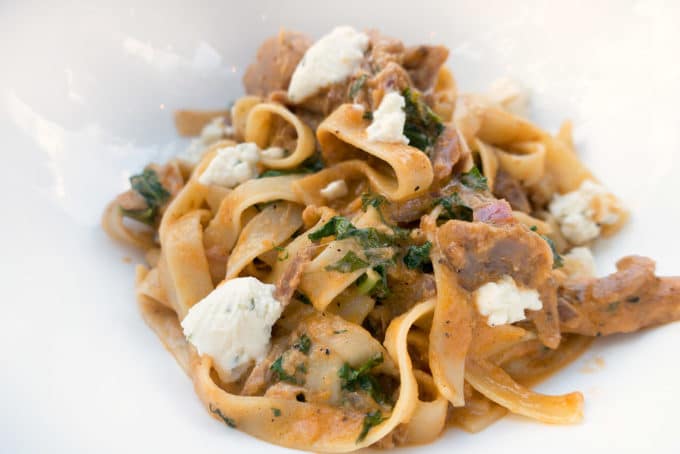 tagliatelli with pulled duck breast in a rosa sauce with chunks of goat cheese served in a white bowl