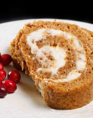 2 slices of pumpkin roll on a white plate with cranberries on a black background