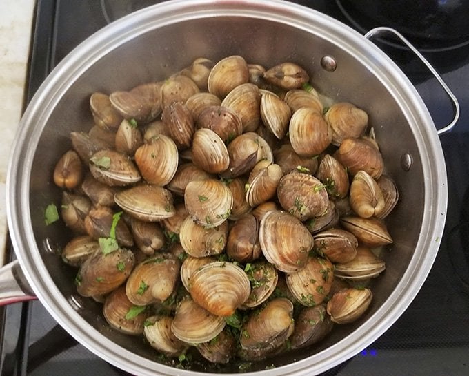 Clams in large pan with seasonings preparing to be steamed.