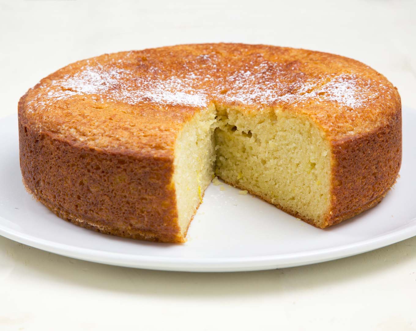 whole orange yogurt cake on a white platter with a large slice cut out 