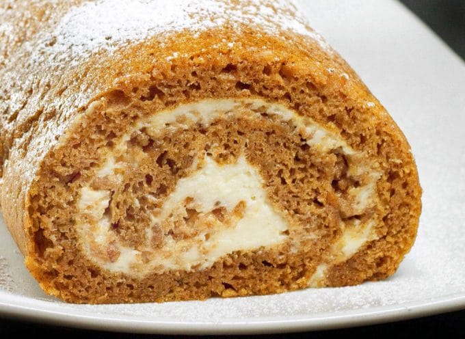 front view of a sliced pumpkin roll on a white plate with a black background