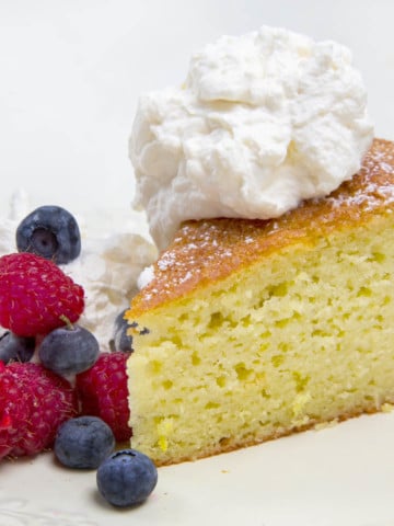 slice of yogurt cake with raspberries and blueberries topped with whipped cream on a white plate