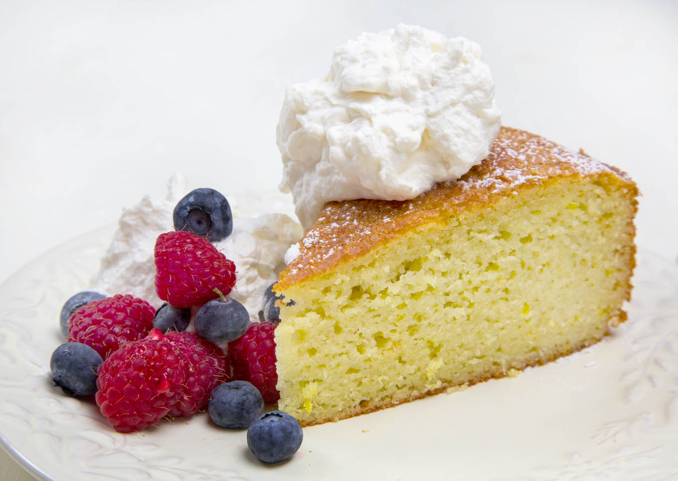 slice of yogurt cake with raspberries and blueberries topped with whipped cream on a white plate