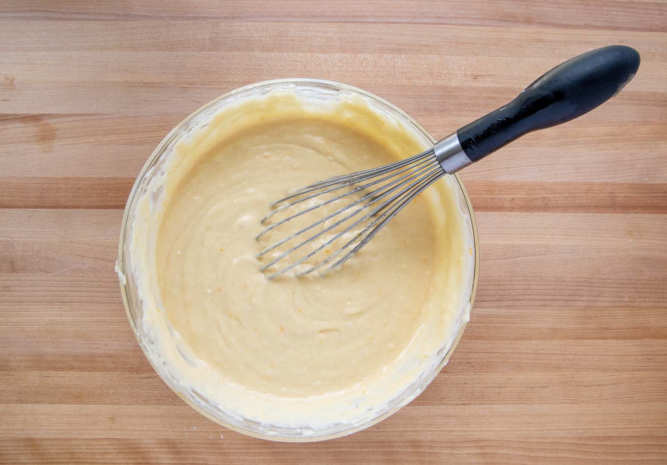 all ingredients mixed together in a glass bowl with a black handled wire whisk in the bowl