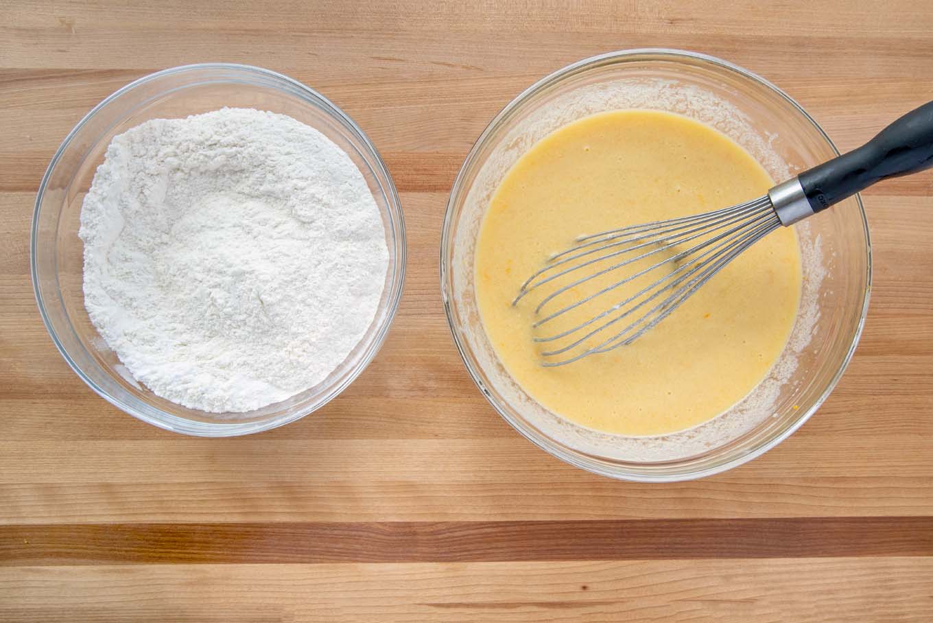 bowl of dry ingredients and bowl of wet ingredients with a black handled wire whisk in the bowl