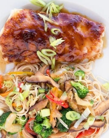 miso glazed cod with stirfried vegetables over noodles on a white plate