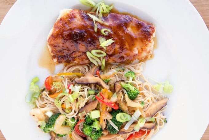 miso glazed cod with stirfried vegetables over noodles on a white plate
