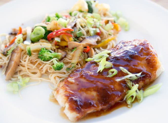 side view of miso glazed cod with stirfried vegetables over noodles on a white plate