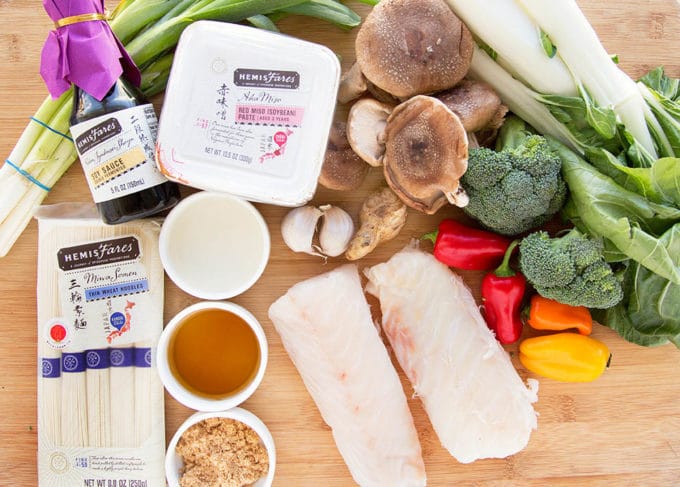 ingredients including vegetables, noodles, miso and fresh cod fillets on a cutting board