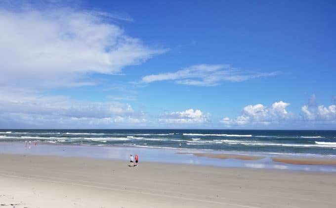 people walking on Daytona Beach by the ocean with beautiful blue skies and puffy white clouds 