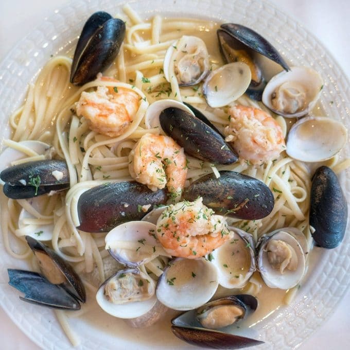 shrimp, mussels and clams over pasta in a garlic aioli sauce in a white bowl