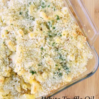white truffle oil cheddar mac and cheese with parsley and bread crumbs in a baking dish, sitting on a cutting board