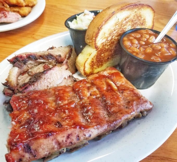 half a rack of ribs, with beef brisket, baked beans, cole slaw and garlic bread on a white plate