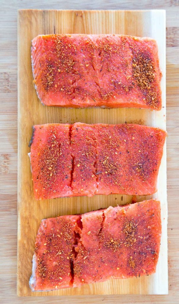 3 pieces of seasoned uncooked salmon on a cedar plank 