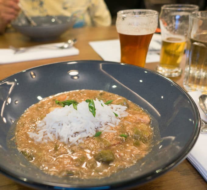 greyish brown gumbo in a dark grey bowl with a pile of white rice in the middle of the bowl. 