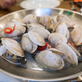 Metal bowl of steamed New England Style Clams in a clam broth with red peppers