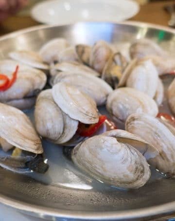 Metal bowl of steamed New England Style Clams in a clam broth with red peppers