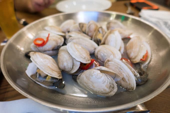 Metal bowl of steamed New England Style Clams in a clam broth with red peppers