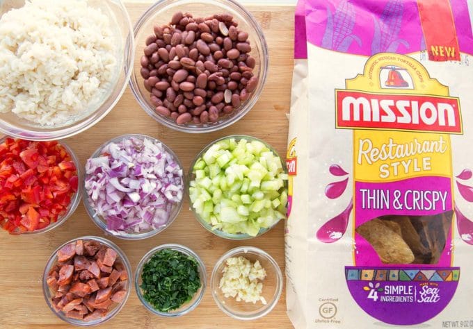 red bean and rice ingredients in bowls with a bag of tortilla chips sitting on a wooden cutting board