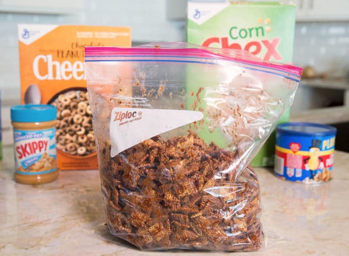 Ziplock bag full of chocolate coated chex cereal with boxes of cereal in the background.