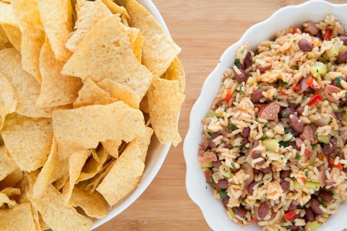 bowl of tortilla chips with a bowl of red beans and rice sitting on a wooden cutting board