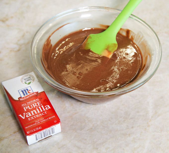 chocolate peanut butter mixture in a glass bowl with a green spatula sticking out of the bowl and a box of pure vanilla sitting on a kitchen counter