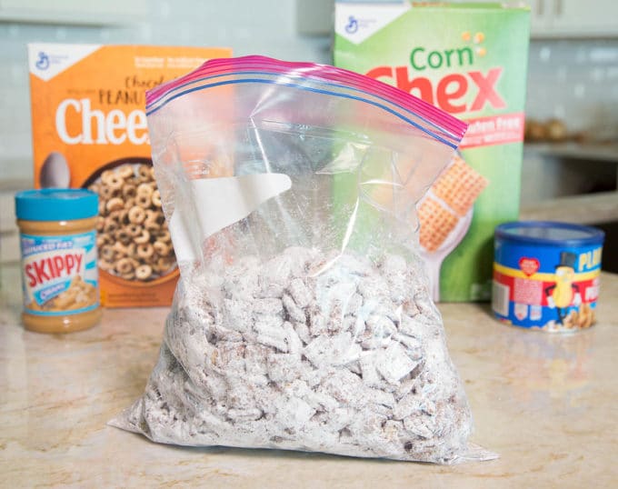 Chex cereal coated in chocolate and confectioners sugar in a ziplock bag sitting on a kitchen counter