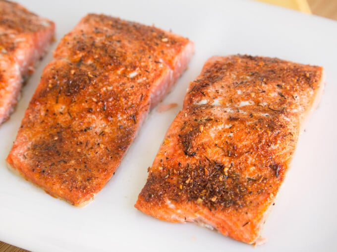 close up of cooked seasoned salmon on a white platter