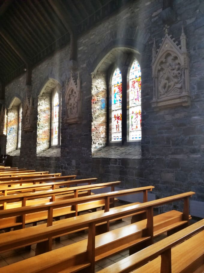 grey stone wall with stained glass windows, light pouring in on wooden peews