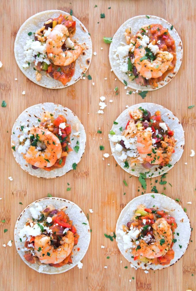 six Etouffee street tacos on a wooden cutting board sprinkled with parsley and Mexican cheese