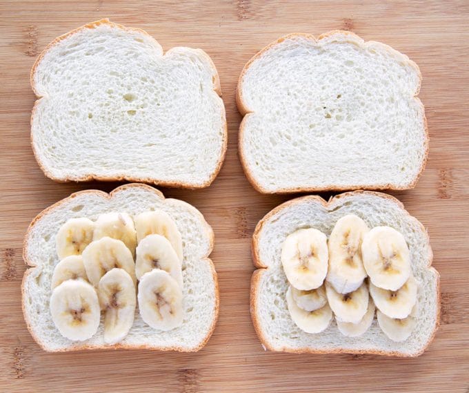 4 slices of thick cut white bread two of which have banana slices on them all sitting on a wooden cutting board