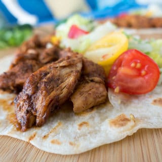 blackened chicken on a flour tortilla with sliced grape tomatoes , shredded lettuce and cheese sitting on a wooden cutting board