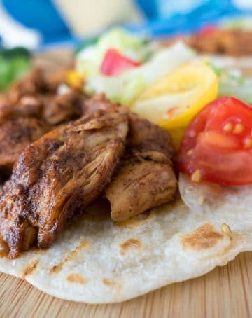 blackened chicken on a flour tortilla with sliced grape tomatoes , shredded lettuce and cheese sitting on a wooden cutting board