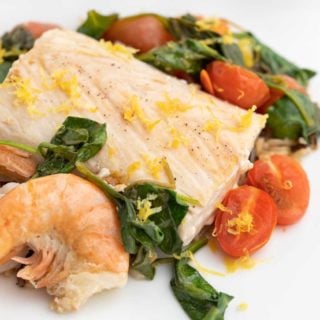 poached mahi-mahi with shrimp on a bed of spinach, tomatoes and rice on a white plate