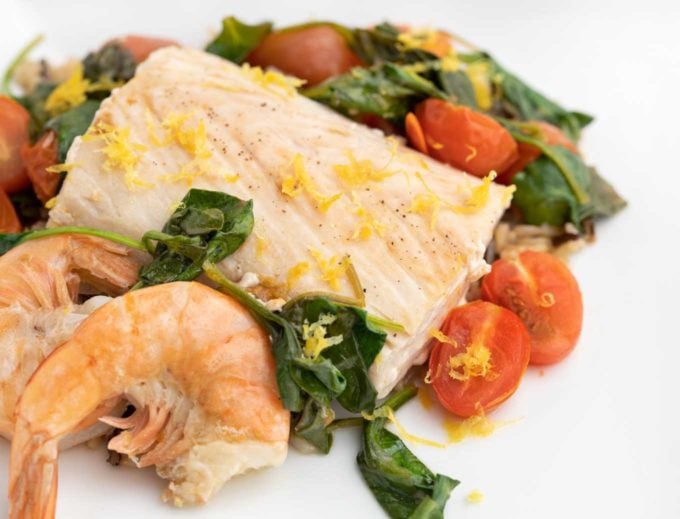 poached mahi-mahi with shrimp on a bed of spinach, tomatoes and rice on a white plate