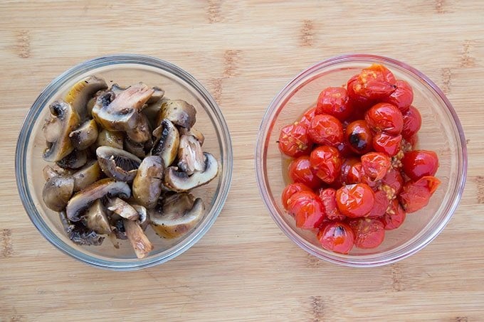 glass bowls of grilled mushrooms and tomatoes on a wooden cutting board