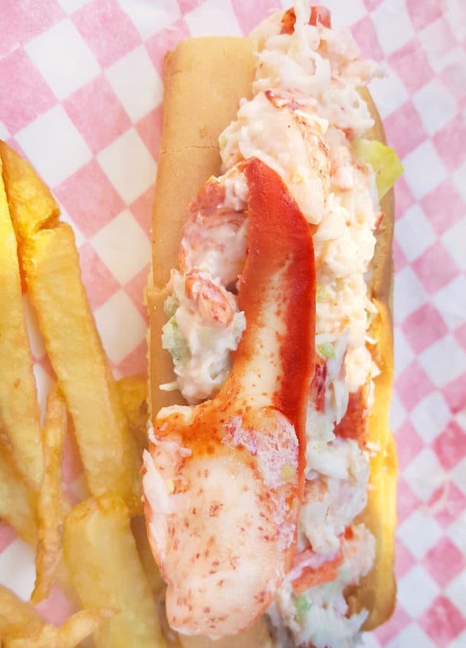 lobster roll sandwich with a large lobster claw on top on a red and white diamond paper with french fries