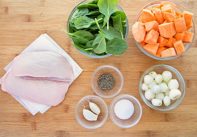 ingredients to make a pan seared duck breast with vegetables sitting on a wooden cutting board. 