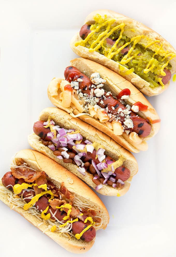 hot dogs with assorted toppings placed diagonally on a white serving tray