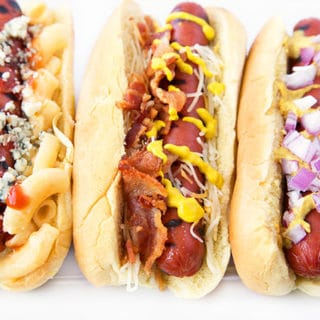 Grilled Hot Dogs on Potato Rolls with different toppings sitting on a White Platter