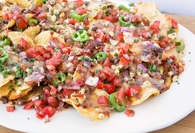 Ultimate Nachos topped with chili and beans, roasted yellow corn kernels, and sliced jalapeños topped with shredded cheddar cheese baked till the cheese is melted!