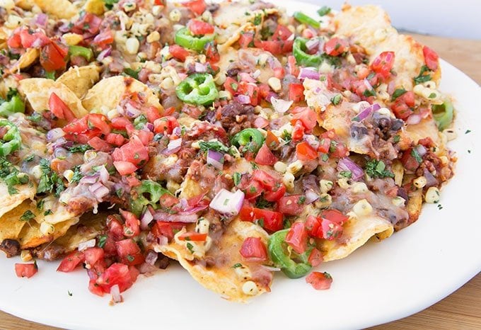 Ultimate Nachos topped with chili and beans, roasted yellow corn kernels, and sliced jalapeos topped with shredded cheddar cheese baked till the cheese is melted!