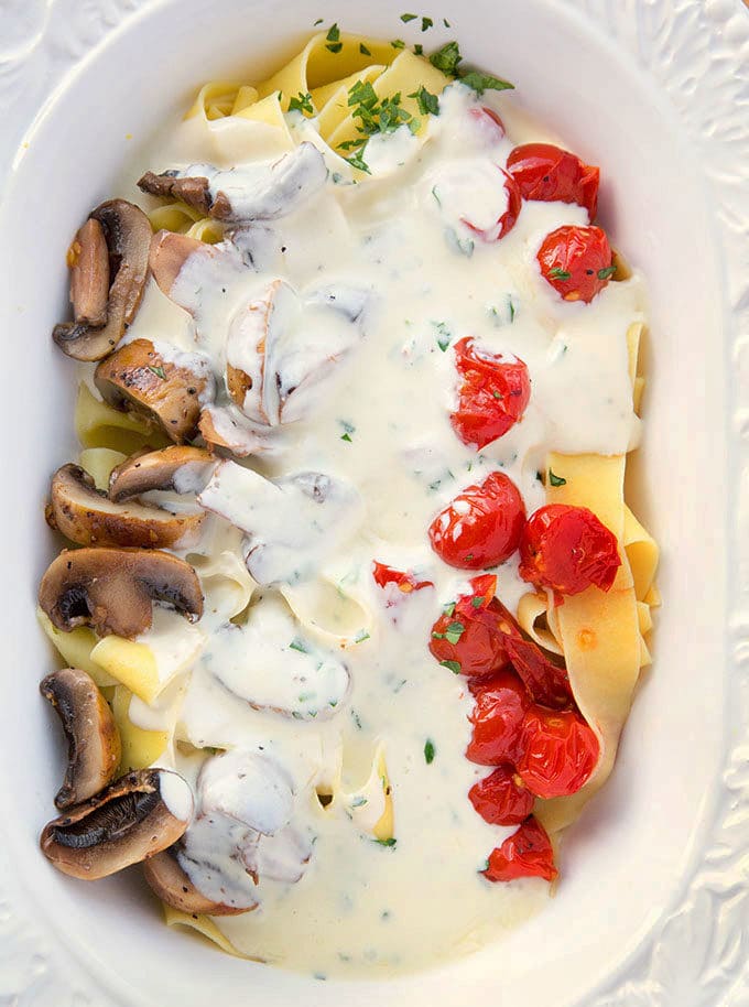 oval white bowl filled with Pappardelle topped with sliced grilled mushrooms, grilled cherry tomatoes and chopped parsley topped with Alfredo sauce