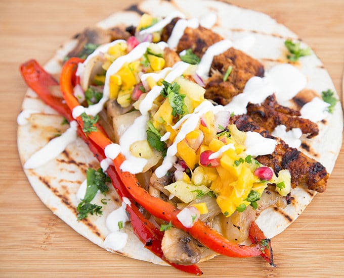 a grilled chicken fajitas topped with pineapple salsa and crema sitting on a wooden cutting board