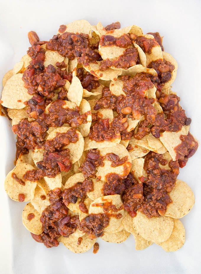 round corn chips topped with 4 bean chili sitting on white parchment paper