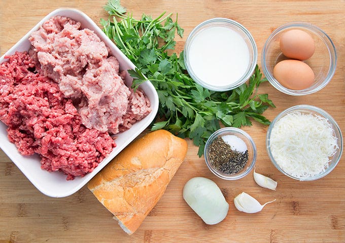 ingredients to make Italian meatballs sitting on a wooden cutting board